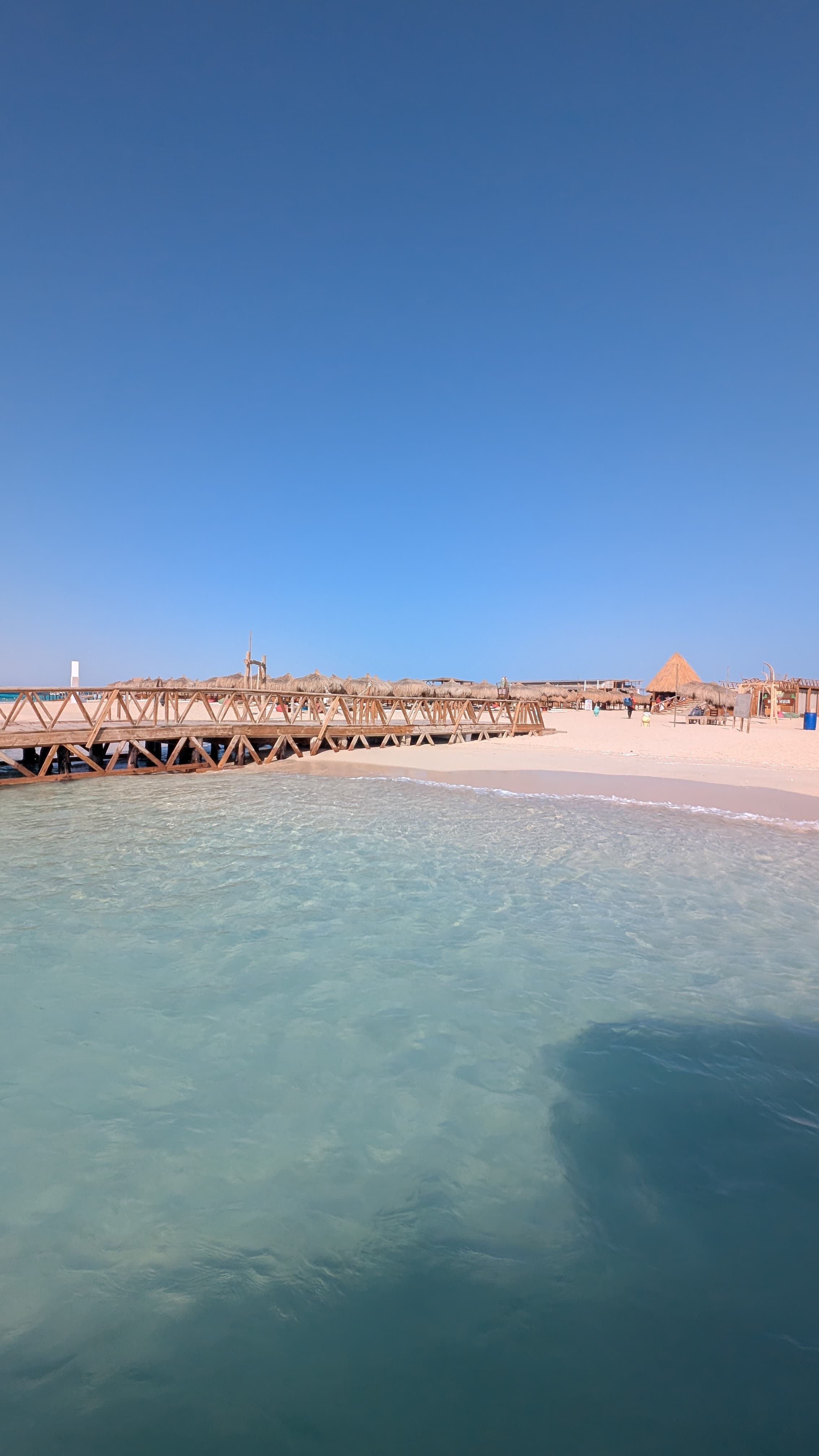 White sand beach with wooden pier and thatched umbrellas on the Red Sea