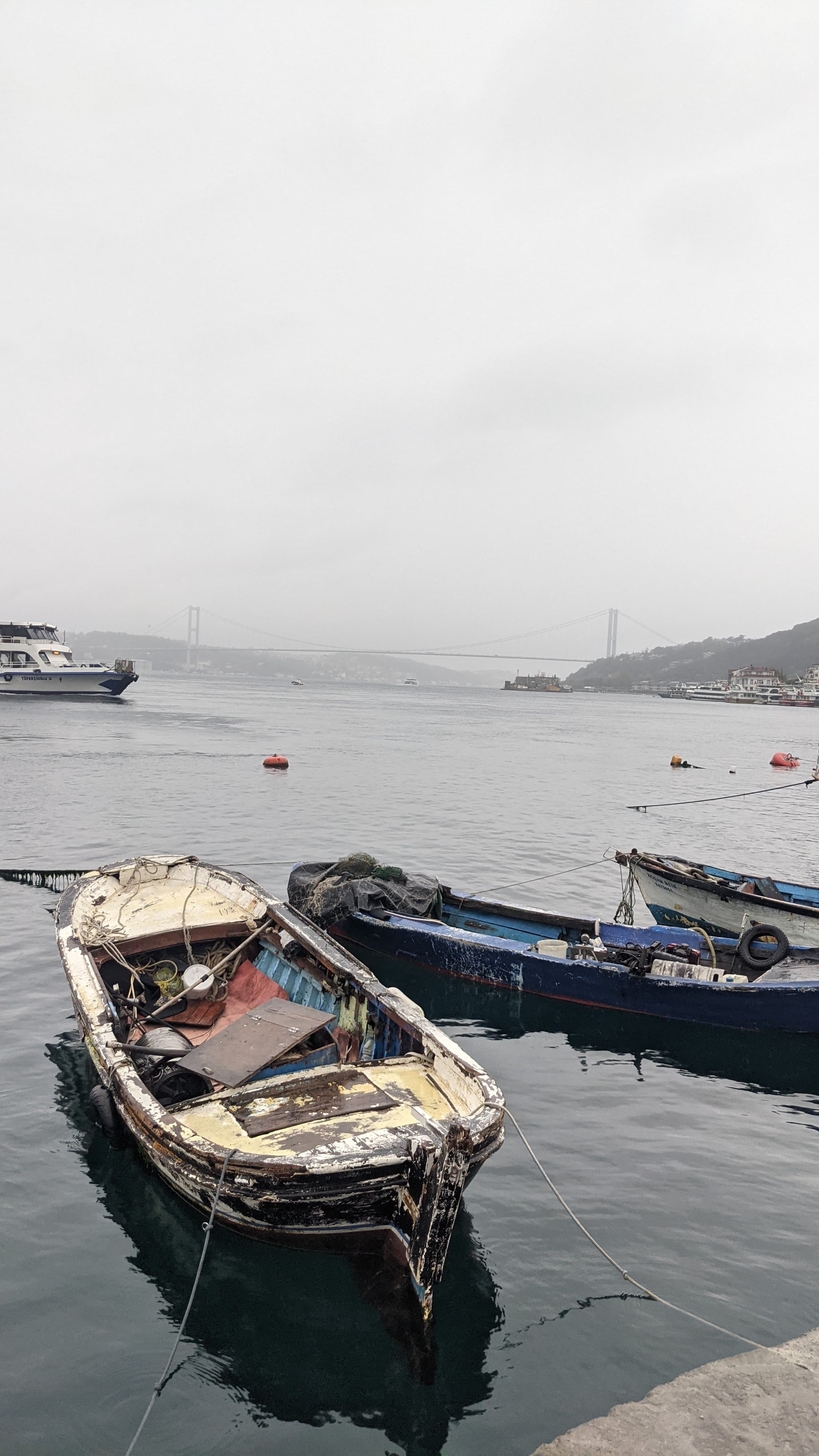 Old boats in the morning mist. The Bosphorus bridge faint in the haze behind them.