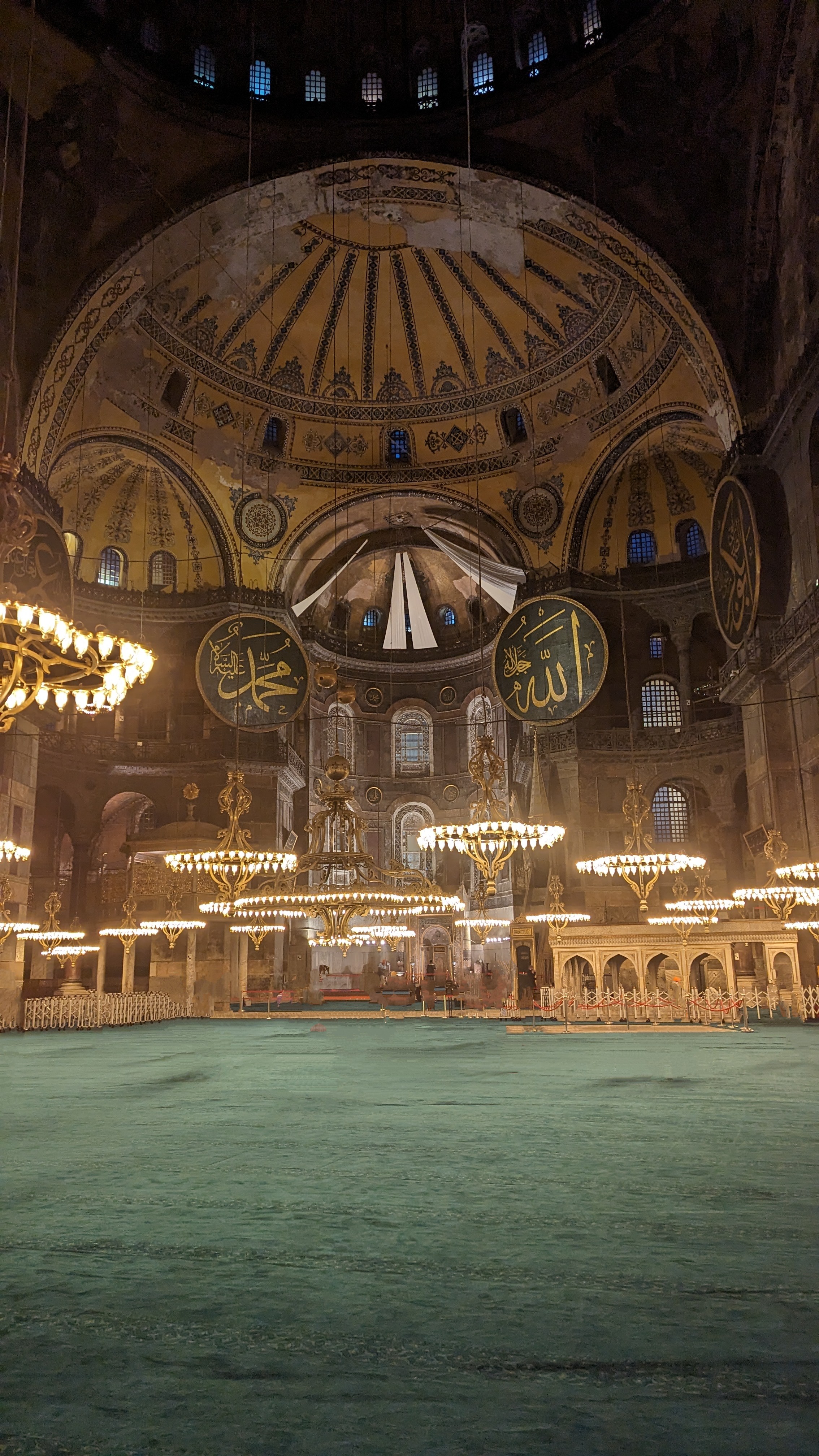 Interior of Hagia Sophia — Byzantine dome, Ottoman calligraphic roundels, golden chandeliers over green prayer carpet